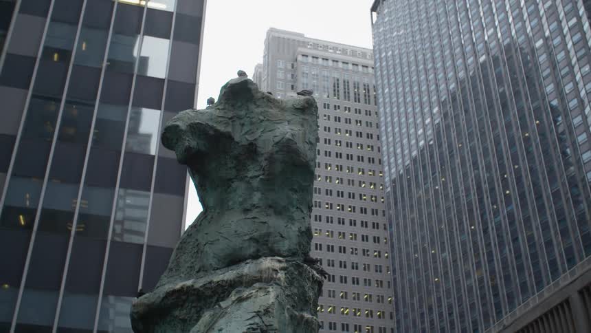 Rough sculptured torso statue stands surrounded by skyscrapers
