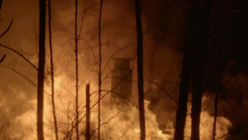 Fire engulfing a building and trees in a wooded area