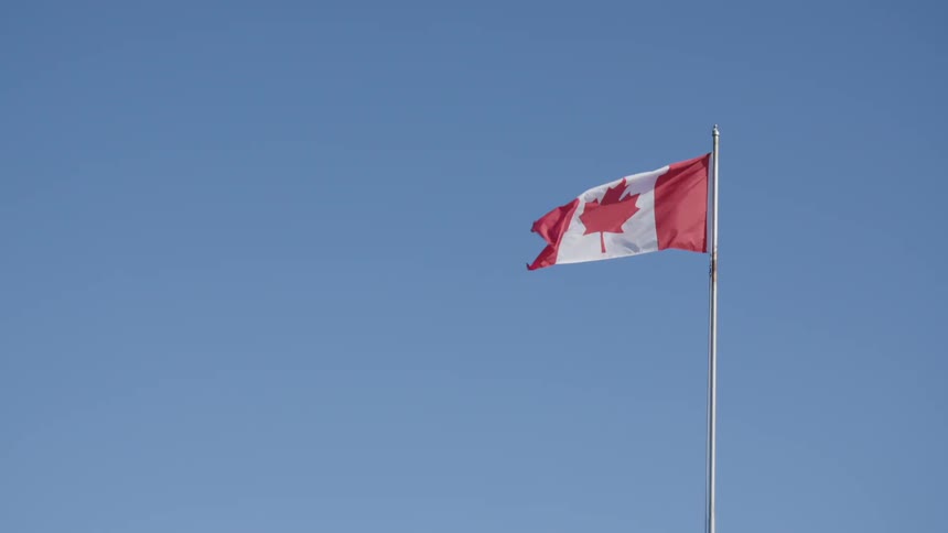A canadian flag on a pole waves in the wind against a bright blue sky