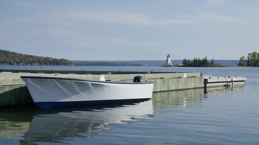 Lighthouse stands on peninsula as boat sits at dock