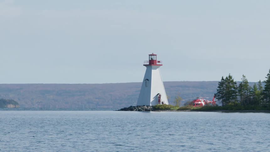 A helicopter sits next to a lighthouse on the shore near the ocean