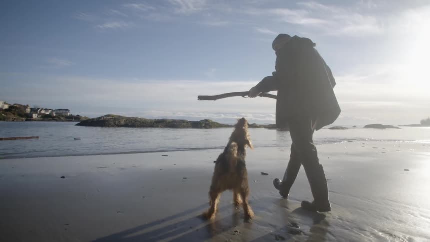 A man is playing with his dog by the water