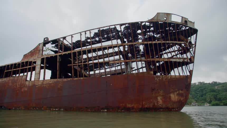 The rusted metal wreckage of a ship on a body of murky water
