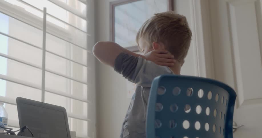 A child sits at a desk and stretches his arms