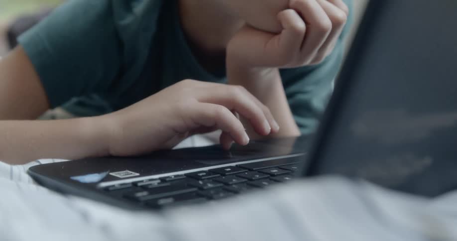 Boy laying in bed uses laptop in bedroom