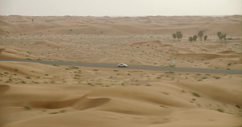 A car drives along a street next to a desert like area