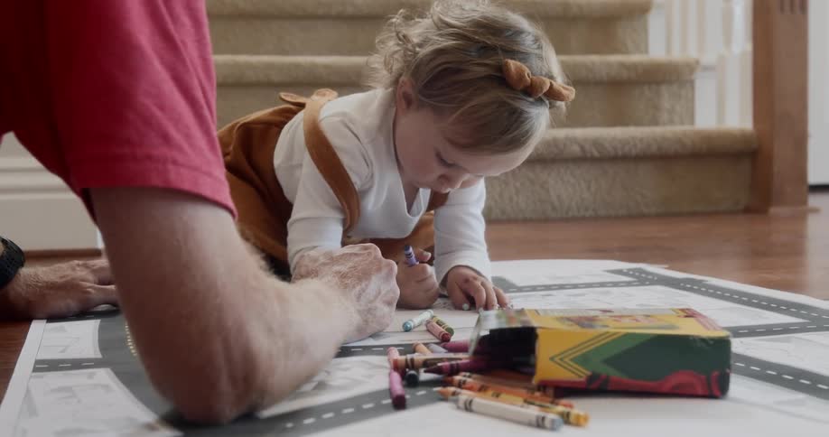 A person and a little girl coloring on paper on the floor with crayons