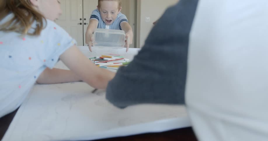 A young girl dumps markers on a table covered in paper for her friends to use