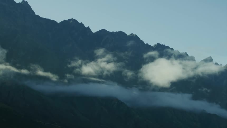 A mountain range with clouds moving nearby
