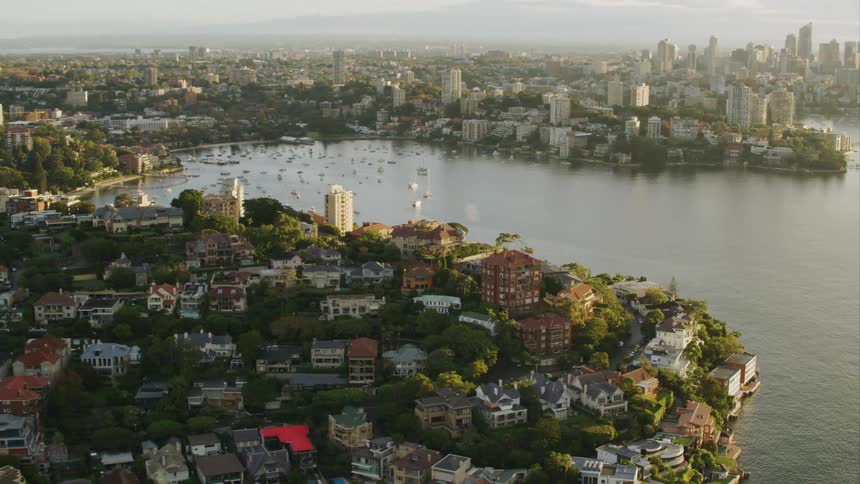 A neighborhood sits on promontory near a bay with a city skyline in the distance Sydney Harbour