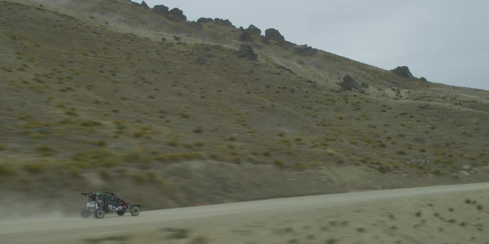 A car is driving midday in a desert area