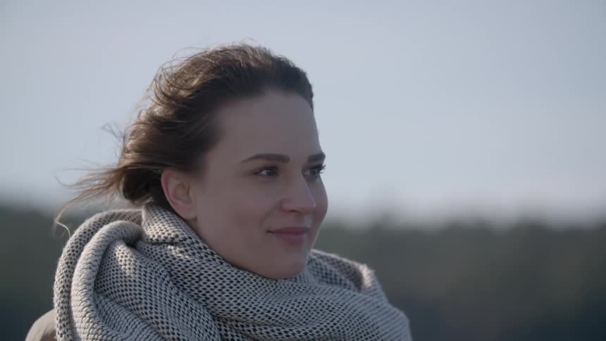 A woman is standing outside smiling on a windy day