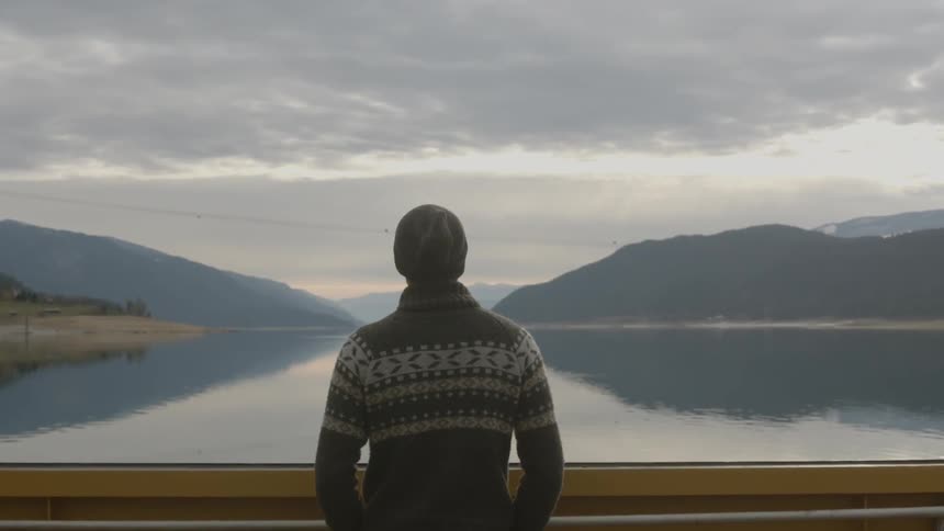 A man looking out over a mountain lake on a cloudy day