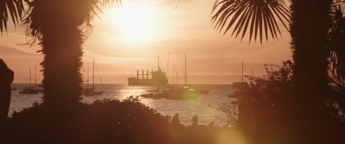 People walk back and forth on shore while boats sit in the ocean offshore