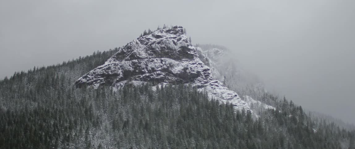 Snow covered mountain surrounded by pine trees and clouds