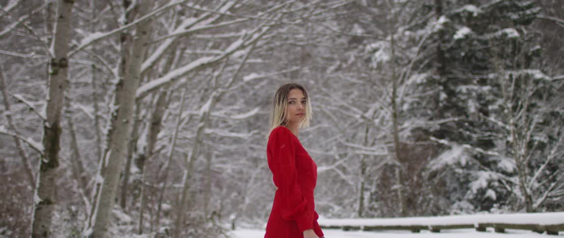 A white woman in a red dress turns around while standing outside in the snow
