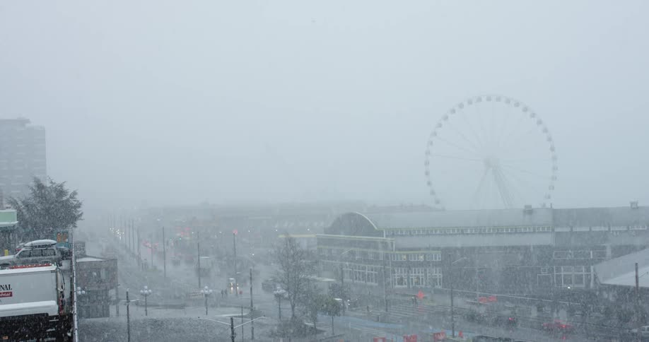 A street with vehicles while it is snowing with a ferris wheel in the background