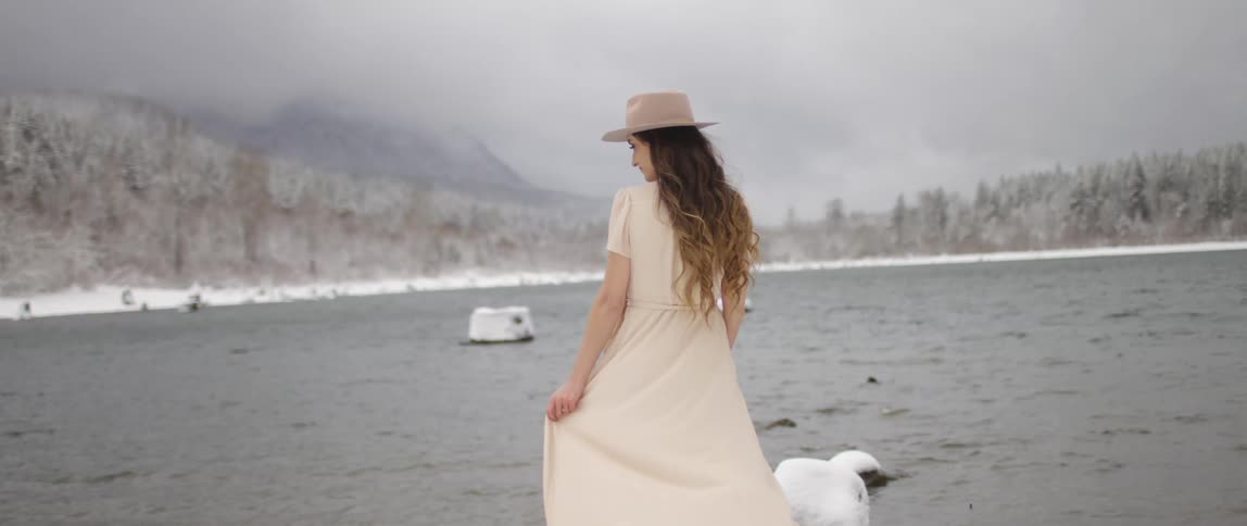 Woman wearing a cream dress stands lakeside