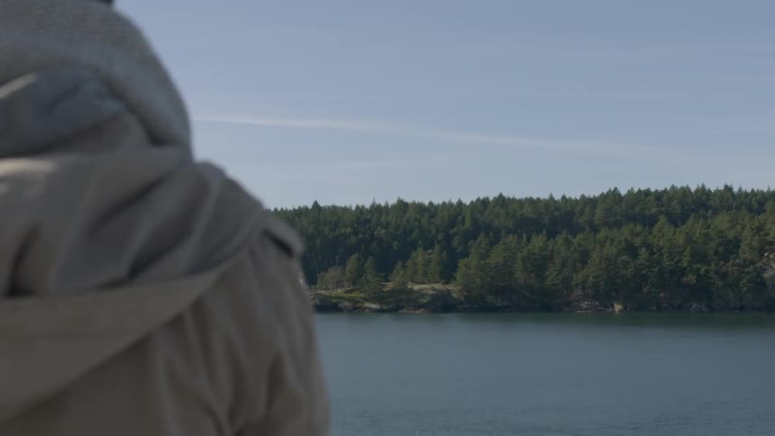 A woman in a light colored jacket looks out at a lake