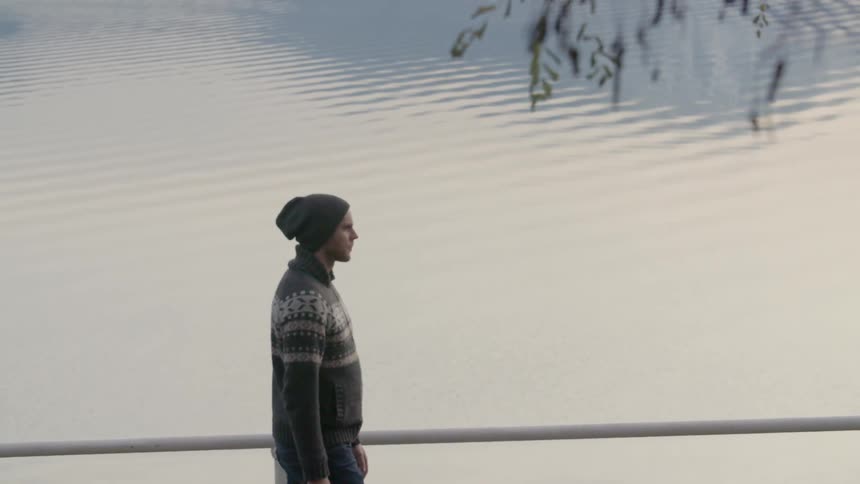 A man is walking along a railing by the water