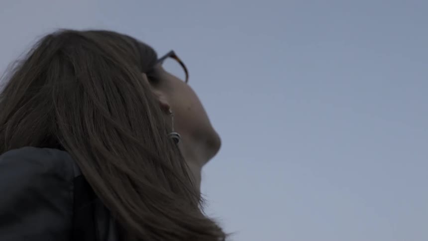A woman standing outside looks up at a light in the sky