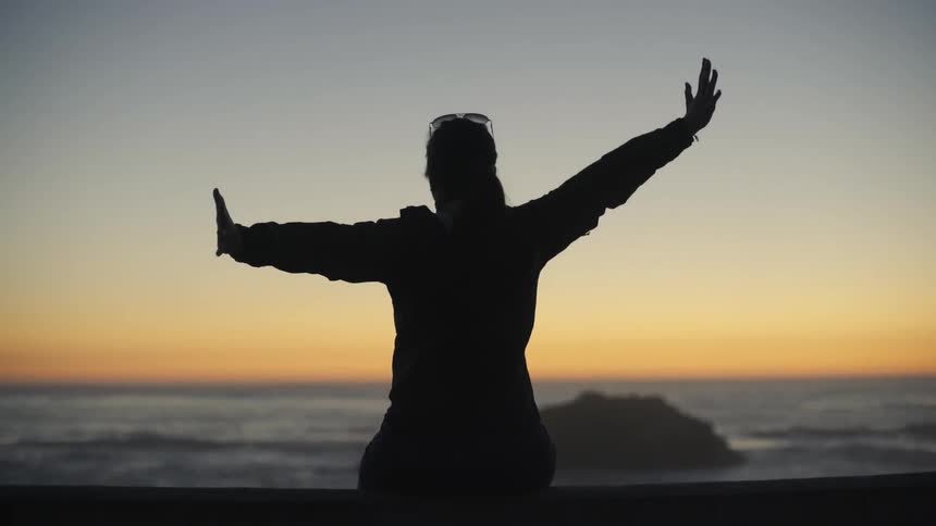 A woman stretching arms open wide watching a sunset