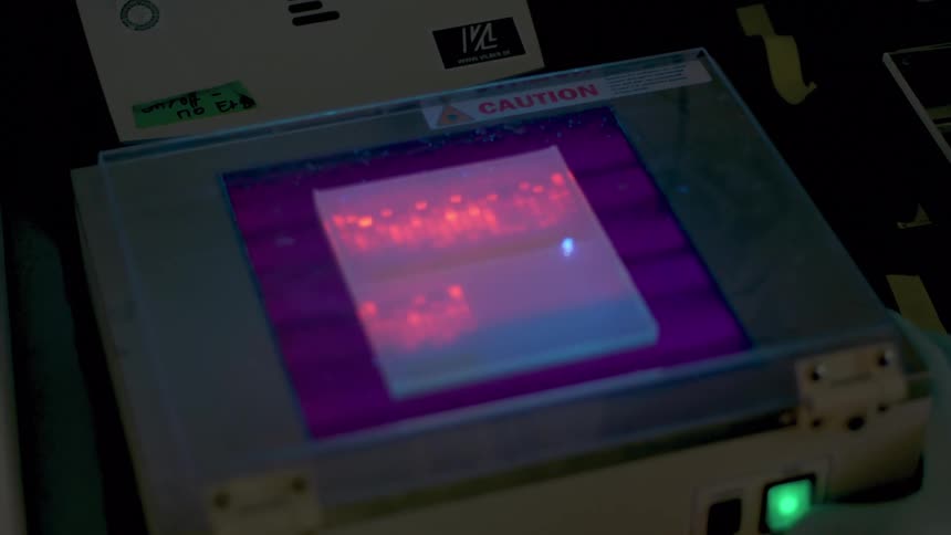 A person wearing rubber gloves works on a machine with a lighted display