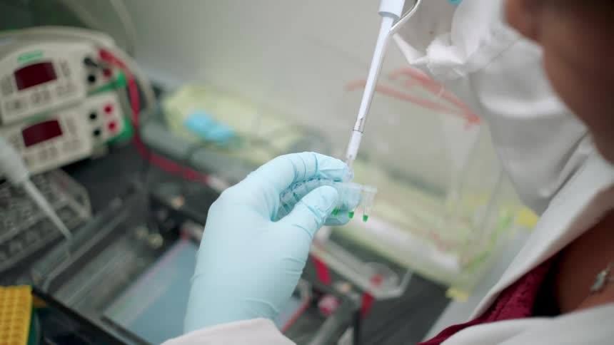 A female lab technician drops fluid into a small cup