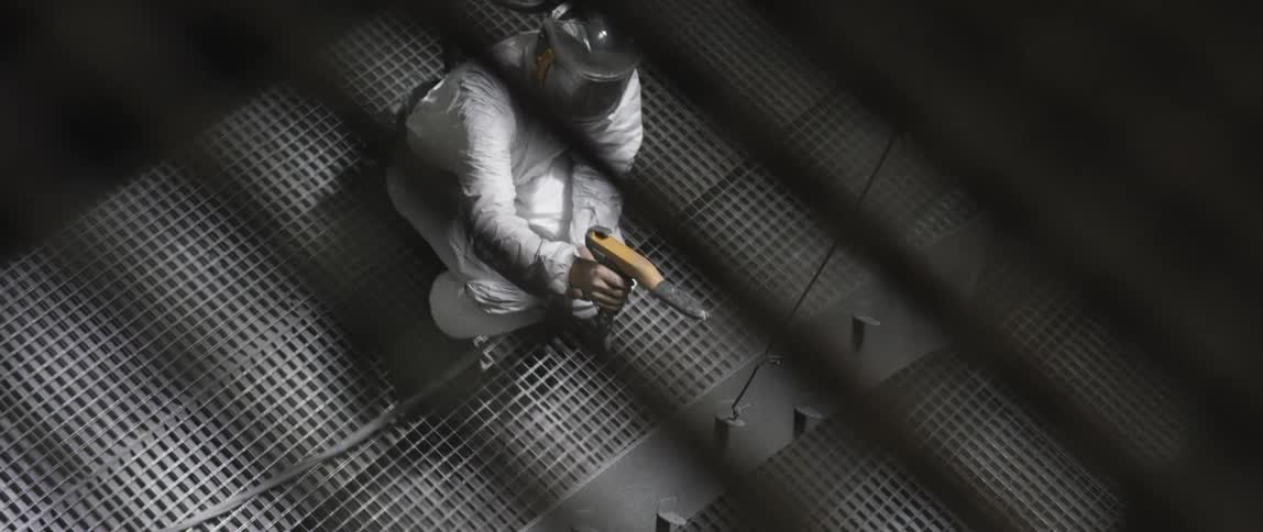 A man in a factory uses a tool to spray metal