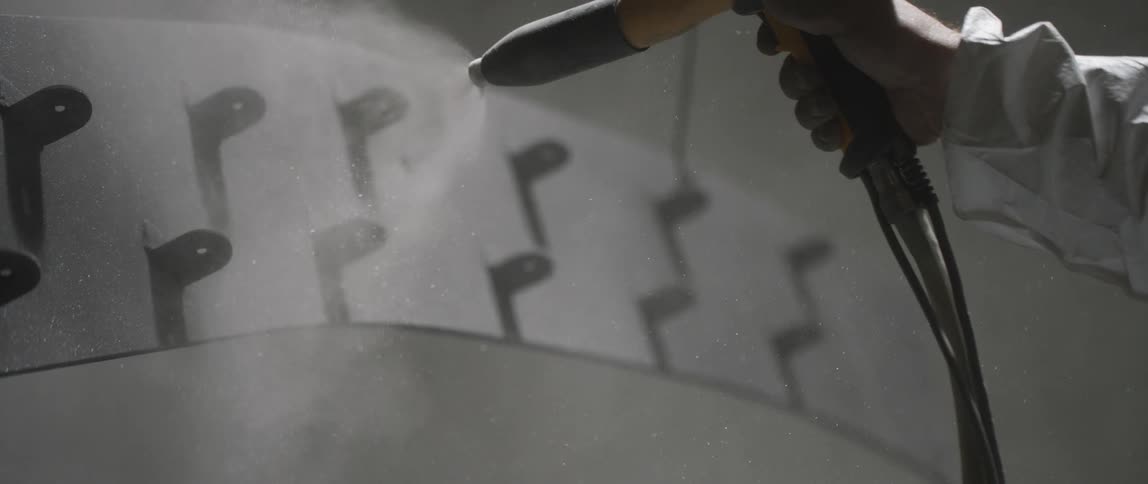 Person spray painting a metal piece inside warehouse
