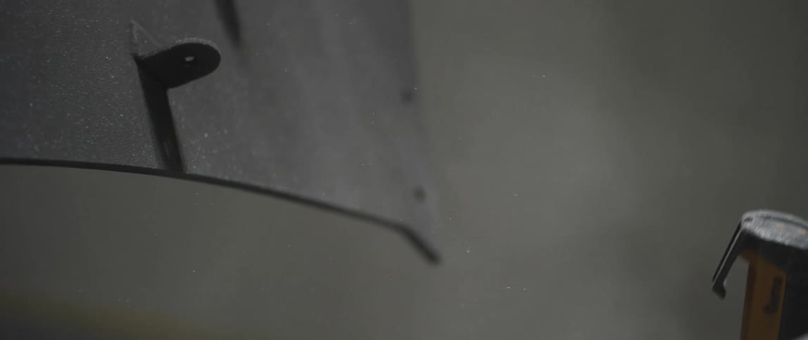 A man uses a power spray gun to paint metal in a workshop