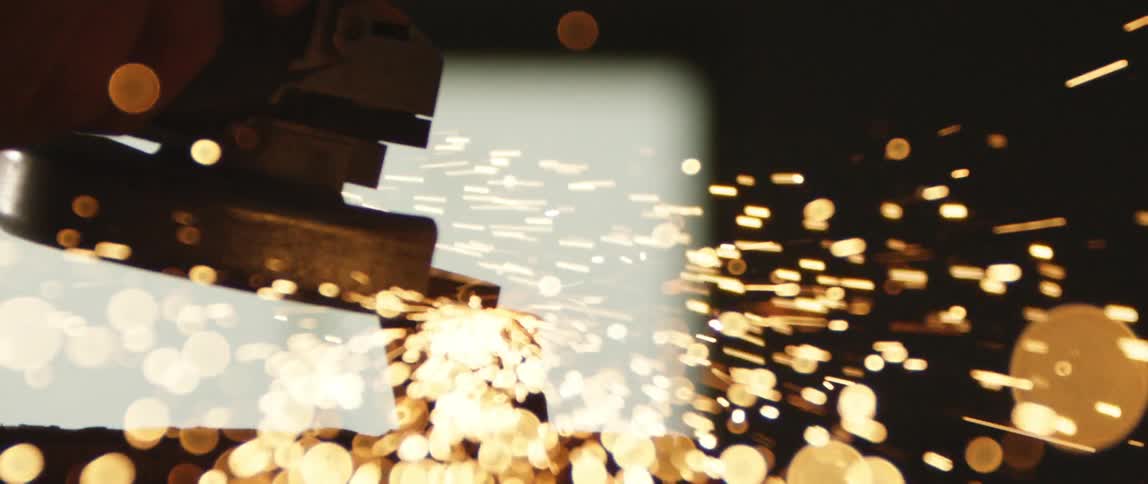 A machine sands a piece of metal and kicks off sparks