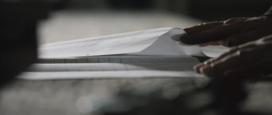 A man smooths pages of plans on a work bench