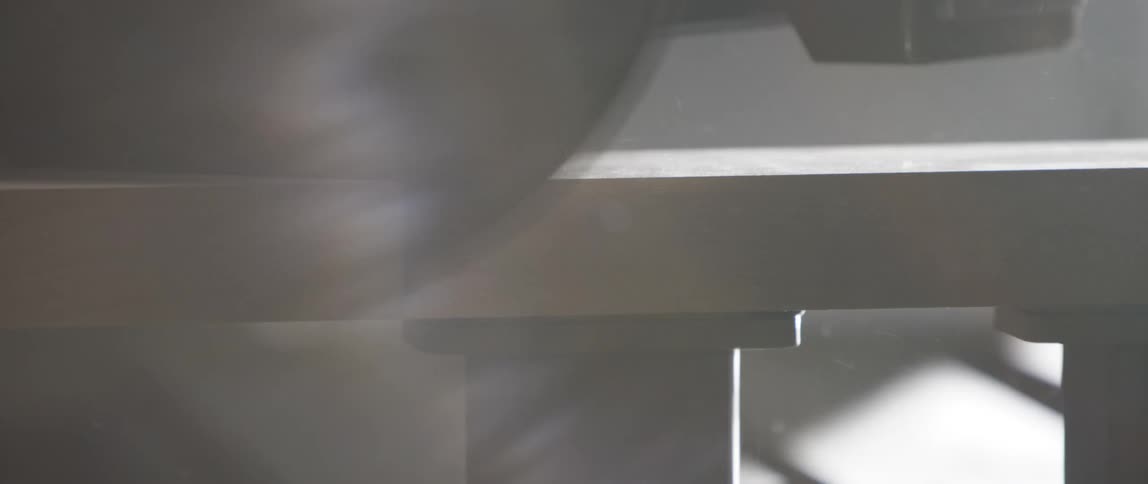 Power saw slices piece of wood in shadowy hazy room