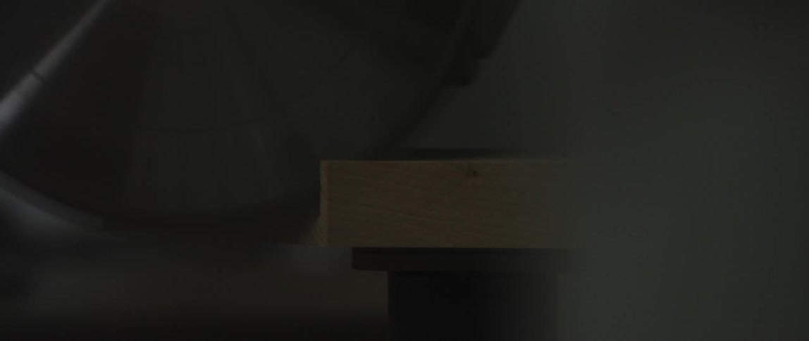 A large circular saw blade cuts through a wooden board