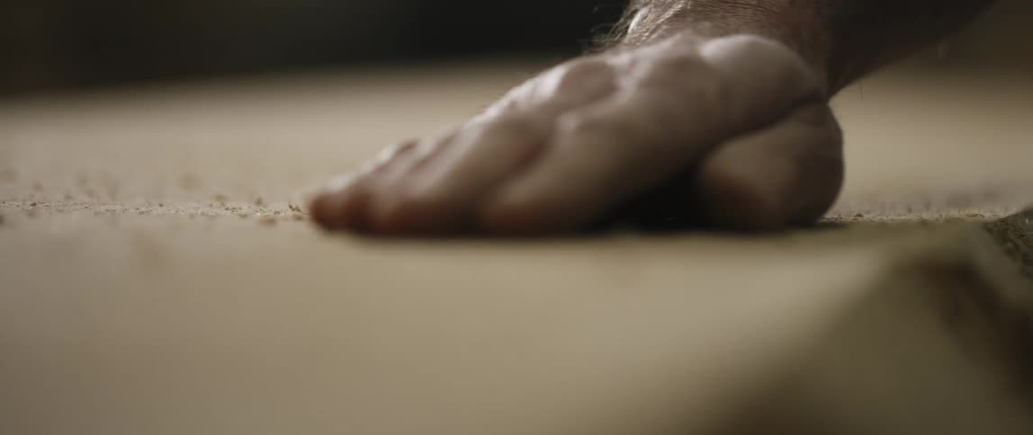 A male hand cleans sawdust off a flat surface