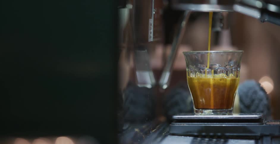 A glass fills up with coffee and a white woman takes it away