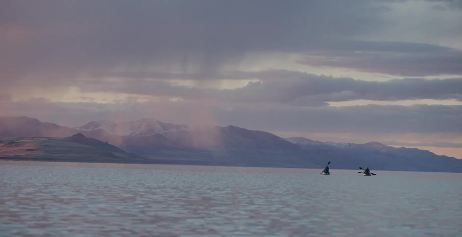 People on kayaks in the ocean at sunrise under stormy clouds