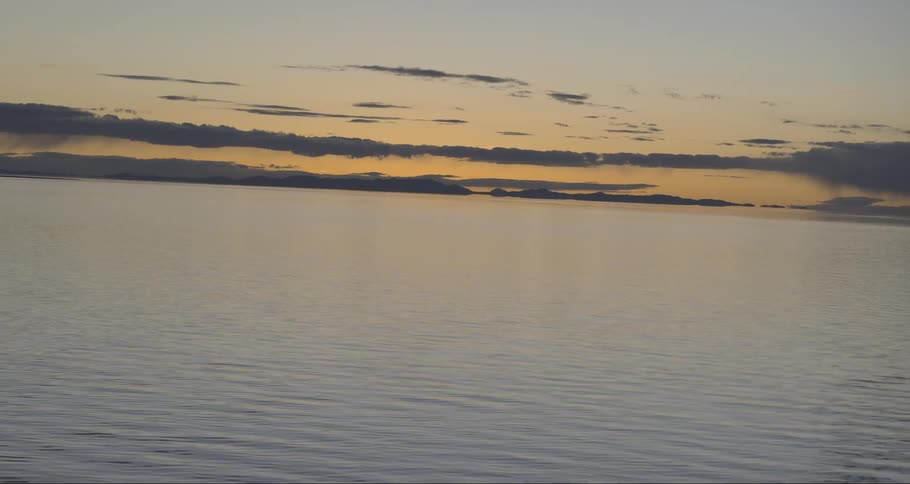 Aerial view of far away mountains from calm sea waters at sunset