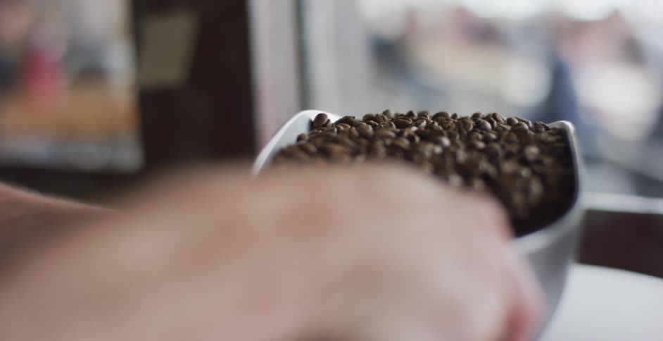 A man in a coffee shop scoops coffee beans on to a scale