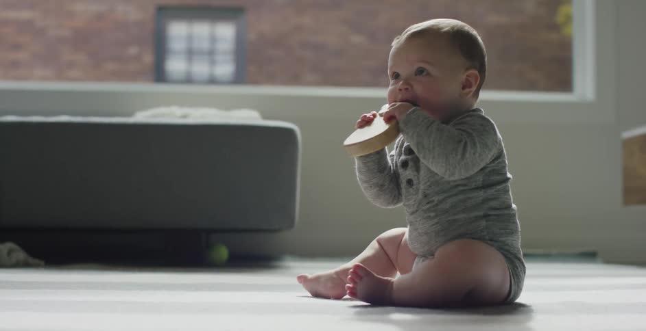 A baby chewing on a wooden toy while sitting on the floor
