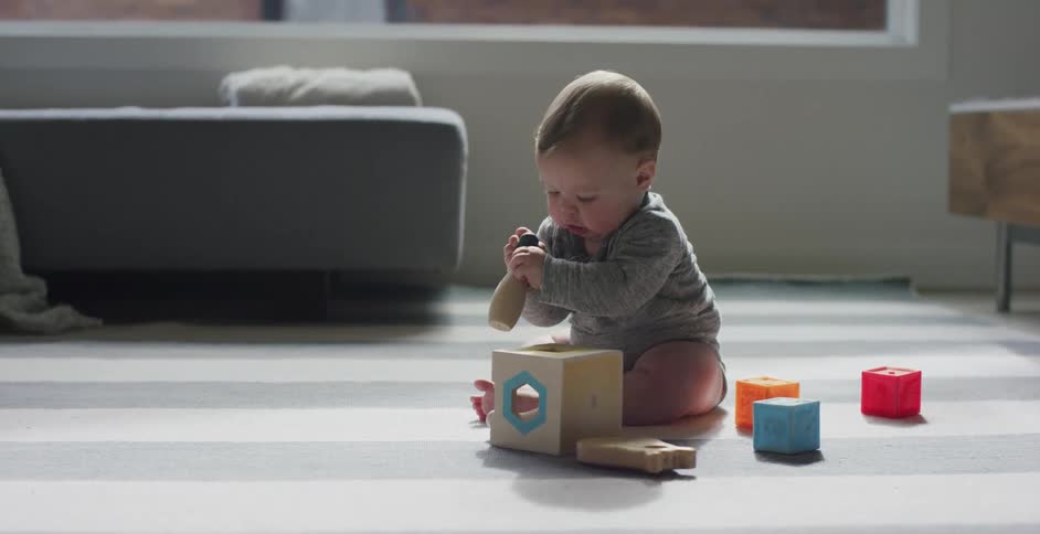 Baby sitting on carpet playing with blocks indoors