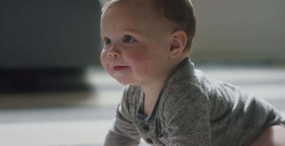 A baby crawls across a floor while drooling