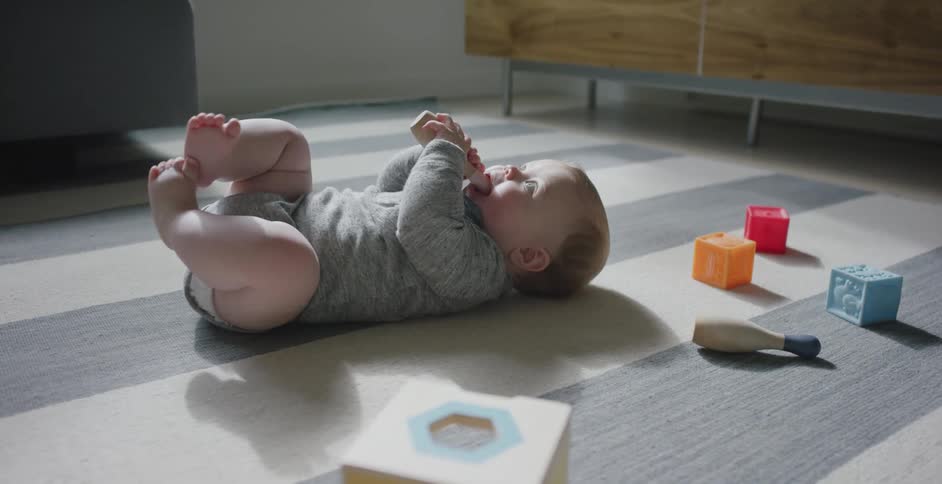 A baby rolls over on a floor covered in toys