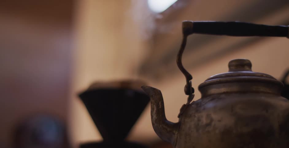 A tea kettle sits on a stove as steam pours out of its spout