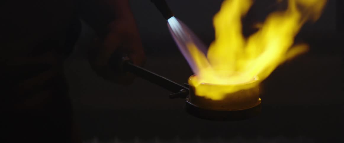 Man uses a torch to melt metal in a crucible 4
