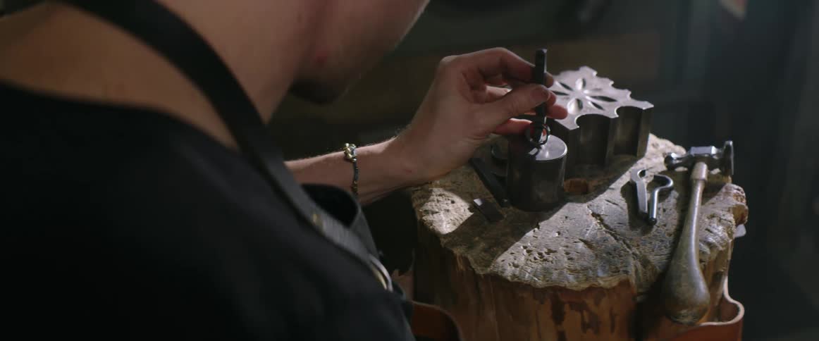 Man wearing apron uses hammer to shape a ring