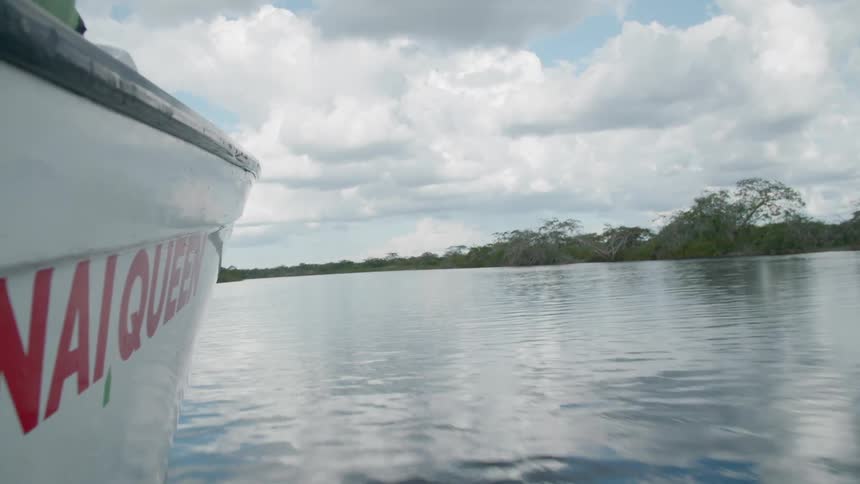 Boat with name painted in red cuts through water near shore