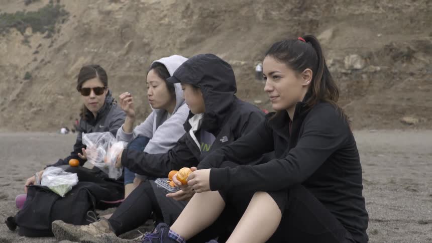 Women enjoying snacks together while sitting on beach in warm golden light.