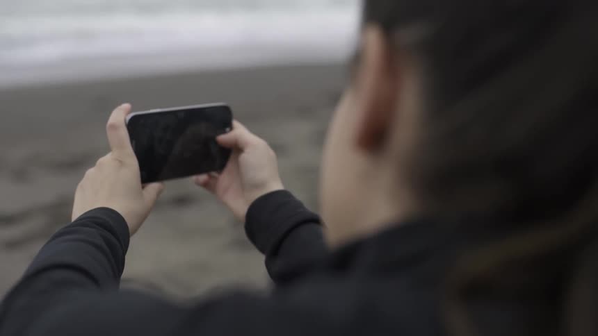 A woman is taking photos by the shore with a phone